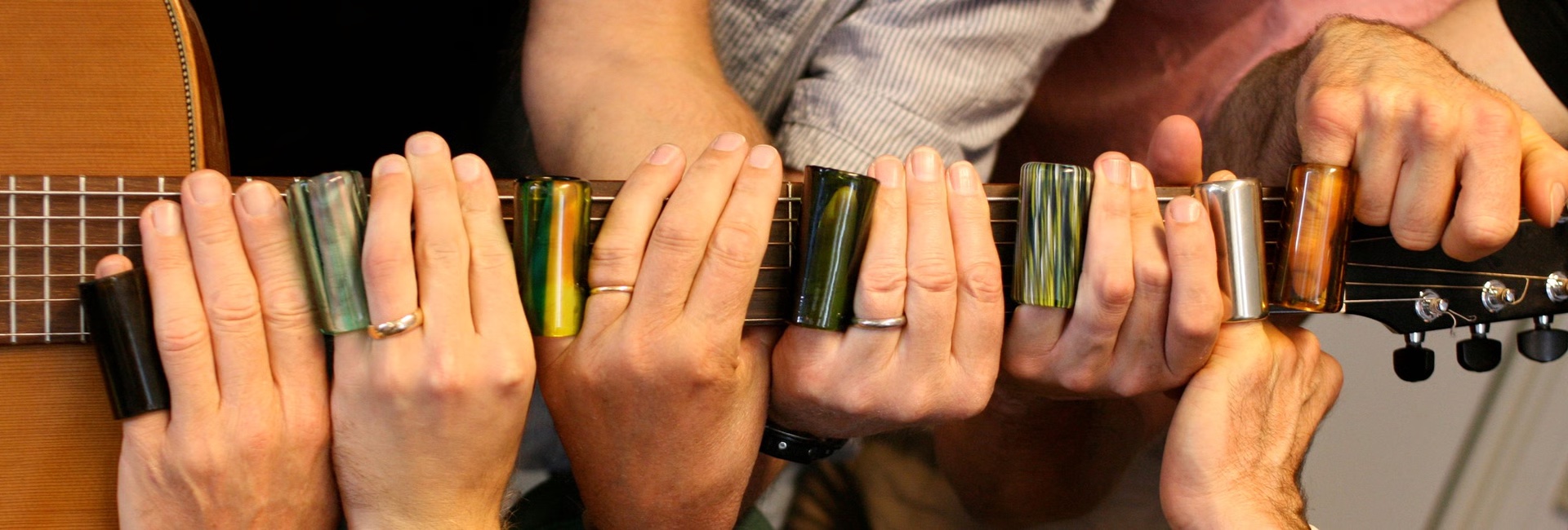 Many hands with guitar slides on the fretboard